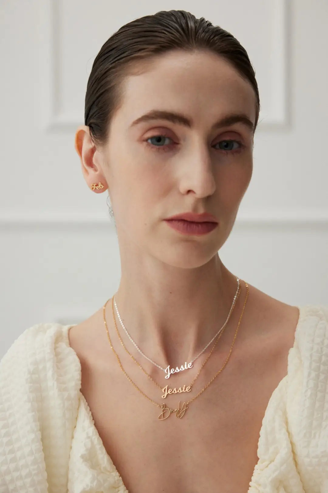 Woman wearing gold jewelry with 'Jesse' and 'Bella' on a plain background