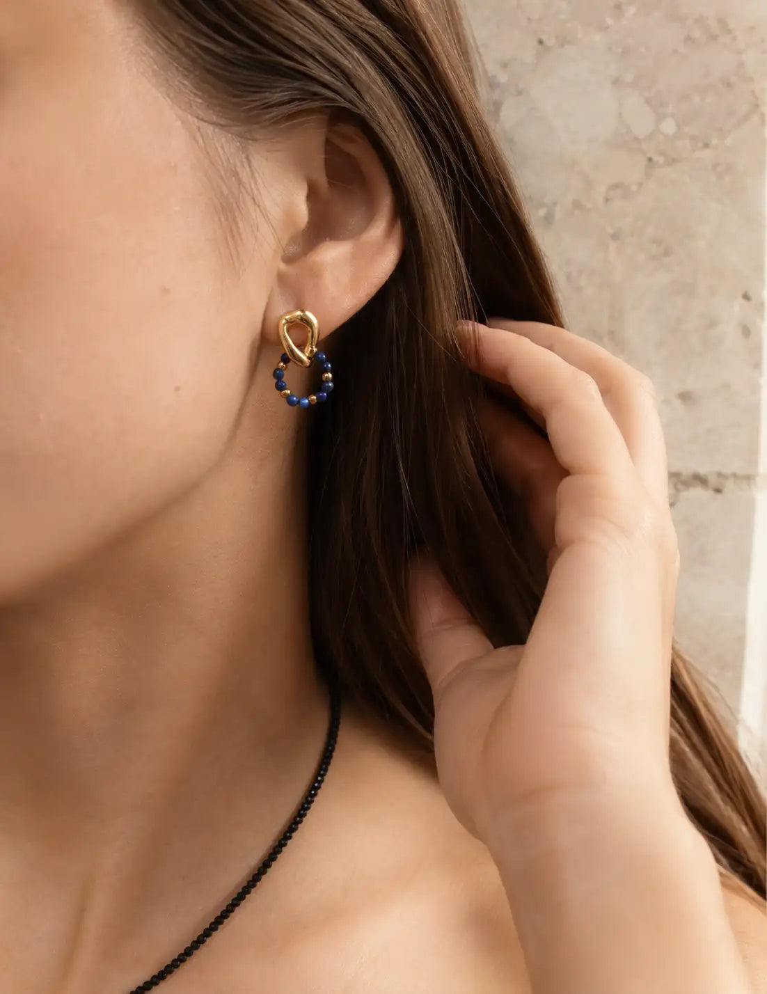 Woman wearing Empires Lapis Lazuli Drop Earrings with 18K gold and blue lapis lazuli stones, styled in a soft garden setting.