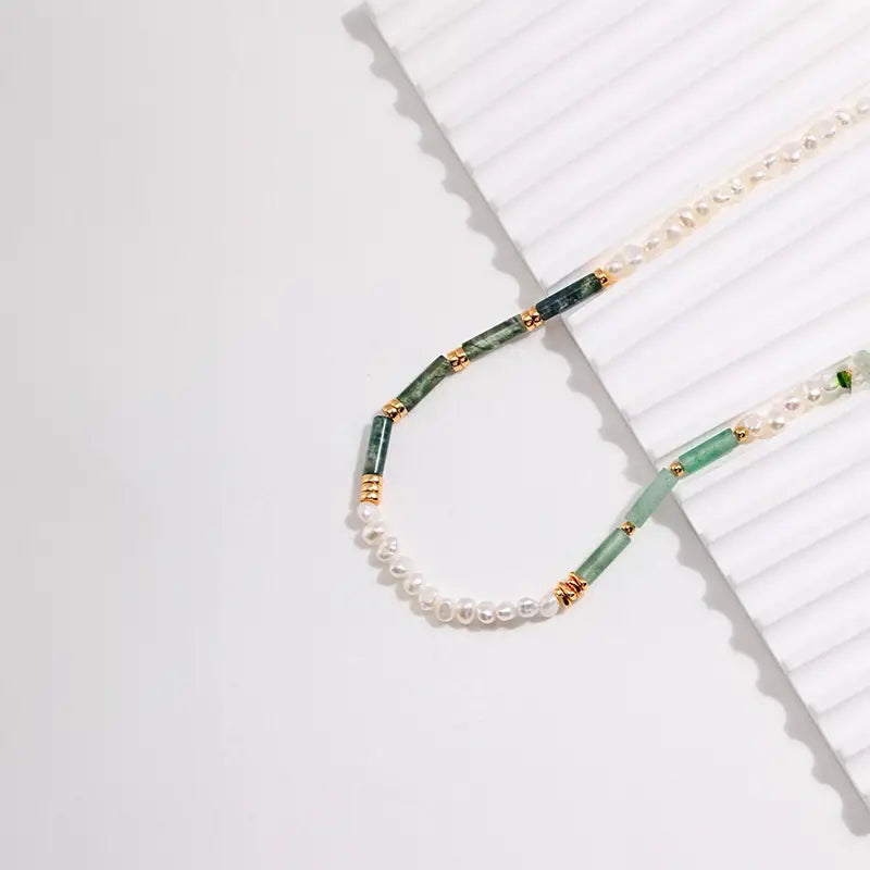 Delicate Aimee Green Crystal Pearl Necklace with gold rings on white ribbed surface.