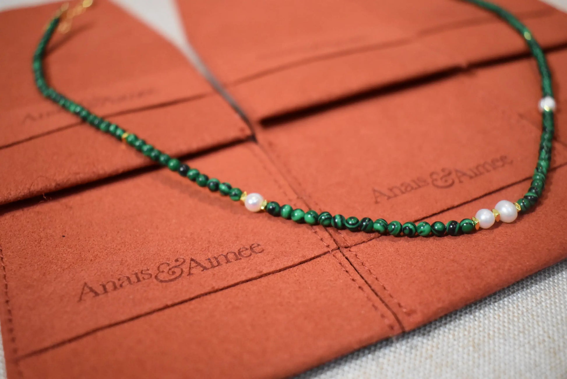Close-up of malachite and freshwater pearl necklace on Anaïs & Aimee branded pouches.
