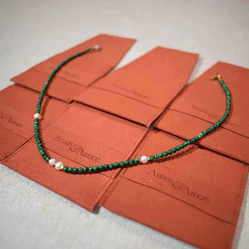 Malachite and freshwater pearl necklace on brown jewelry pouches with gold-plated details.