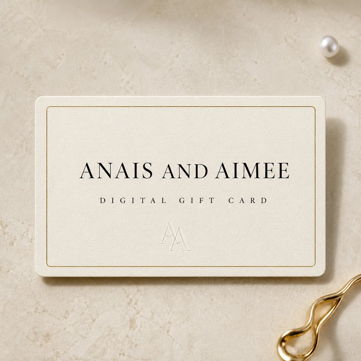 A rectangular cream-colored gift card with gold border lines and black text reading 'ANAIS AND AIMEE' and 'DIGITAL GIFT CARD,' placed on a light beige textured surface with a pearl and gold clip as styled props.