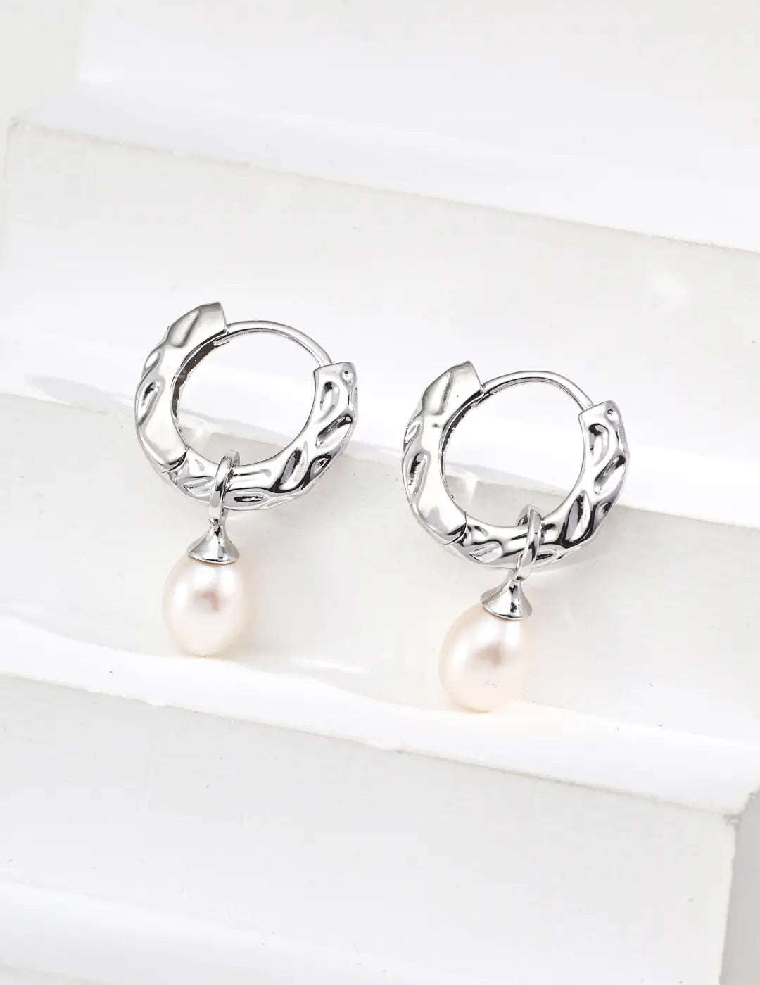 Silver hoop earrings with pearl drops on a white background