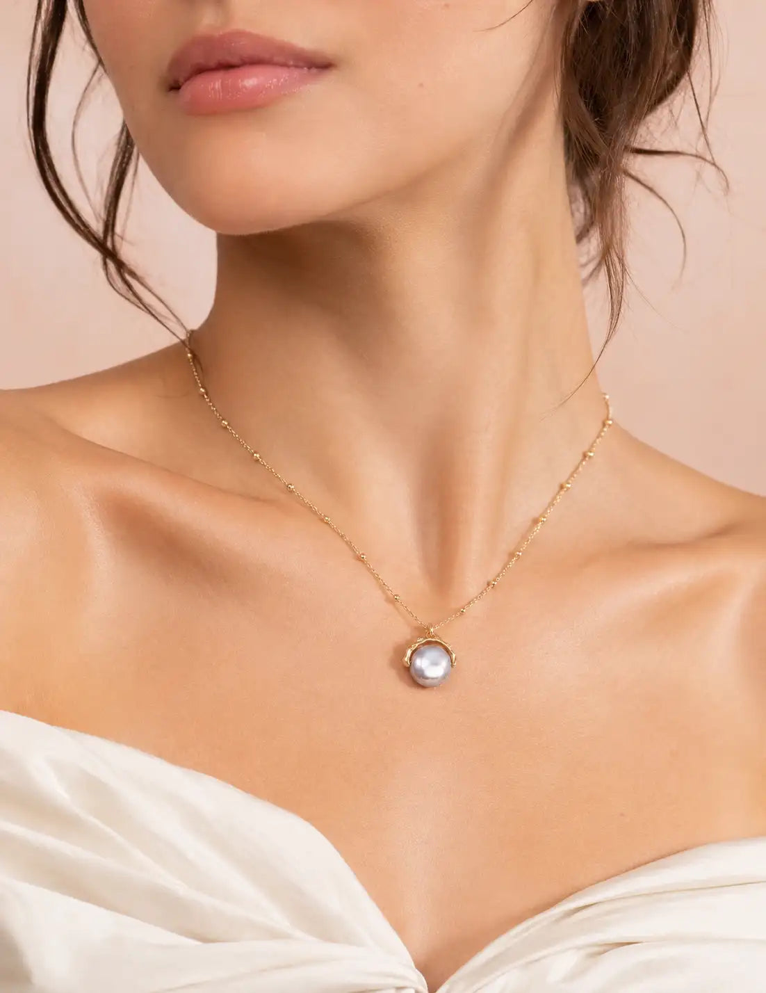 Woman wearing the Ashtead Pearl Pendant Necklace, a delicate gold pearl necklace with a luminous pearl pendant, styled with a white outfit for elegant everyday jewellery.