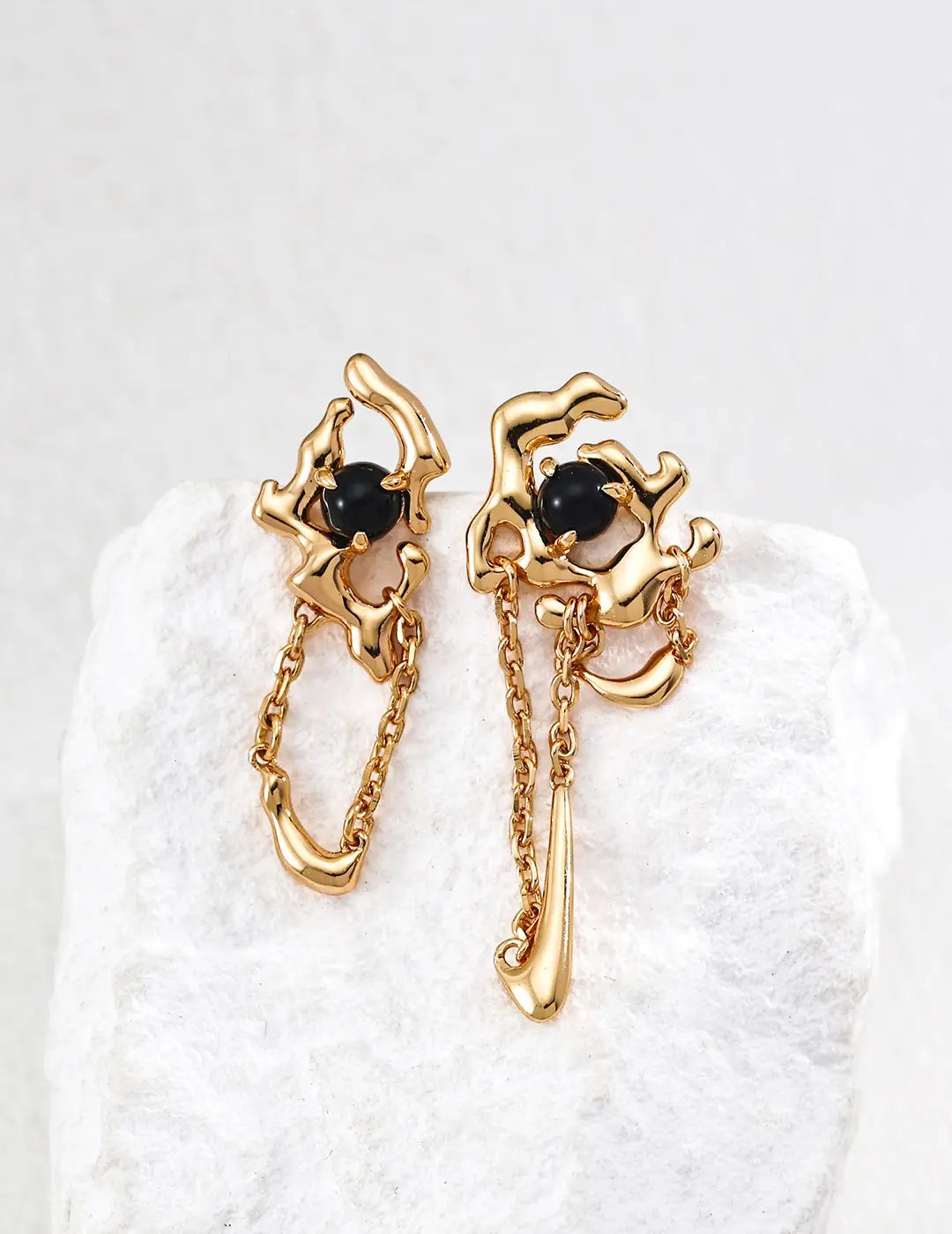 Gold earrings with black stones on a white textured background