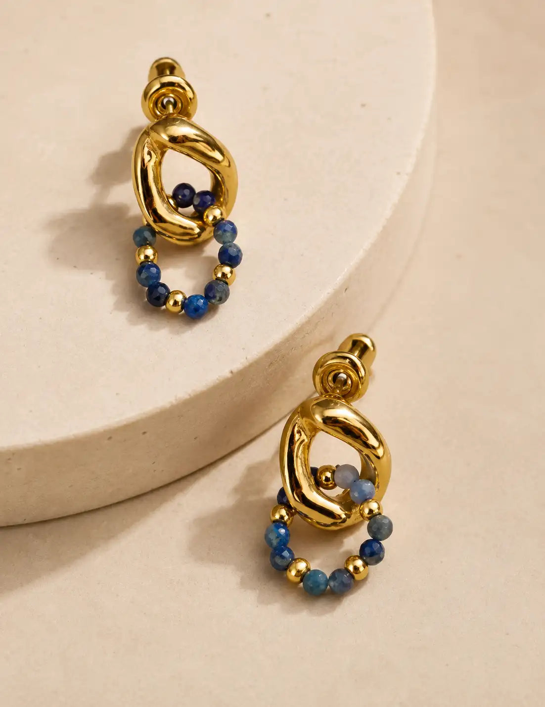 Close-up of Empires Lapis Lazuli Drop Earrings with 18K gold sculptural hoops and blue lapis lazuli bead details worn on the ear.