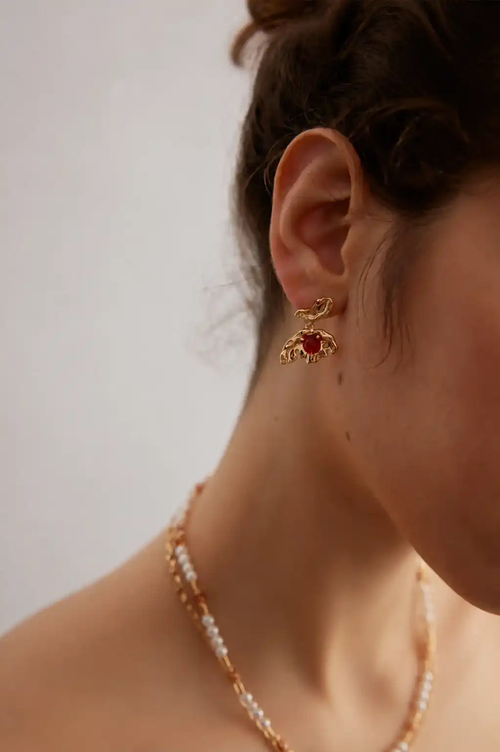 Detailed ear-level view showing the sculptural gold butterfly design and deep-red agate stone against a softly blurred background.