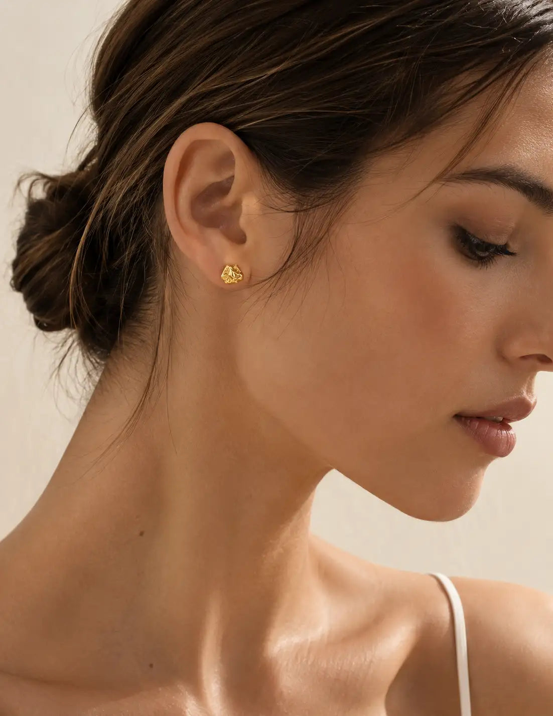 Detailed close-up of small textured gold stud earrings worn on the ear, highlighting the organic surface finish and polished gold colour.