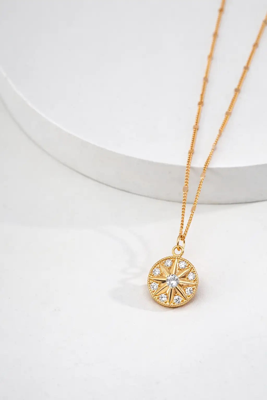 Gold necklace with a circular pendant on a white background