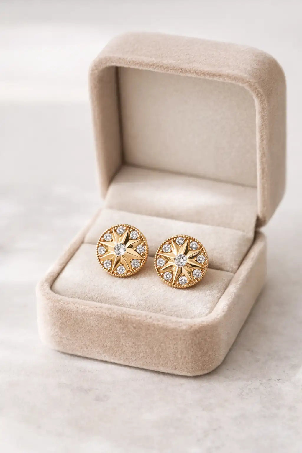 Didcot Gold Earrings with star designs in a beige jewelry box on a light background