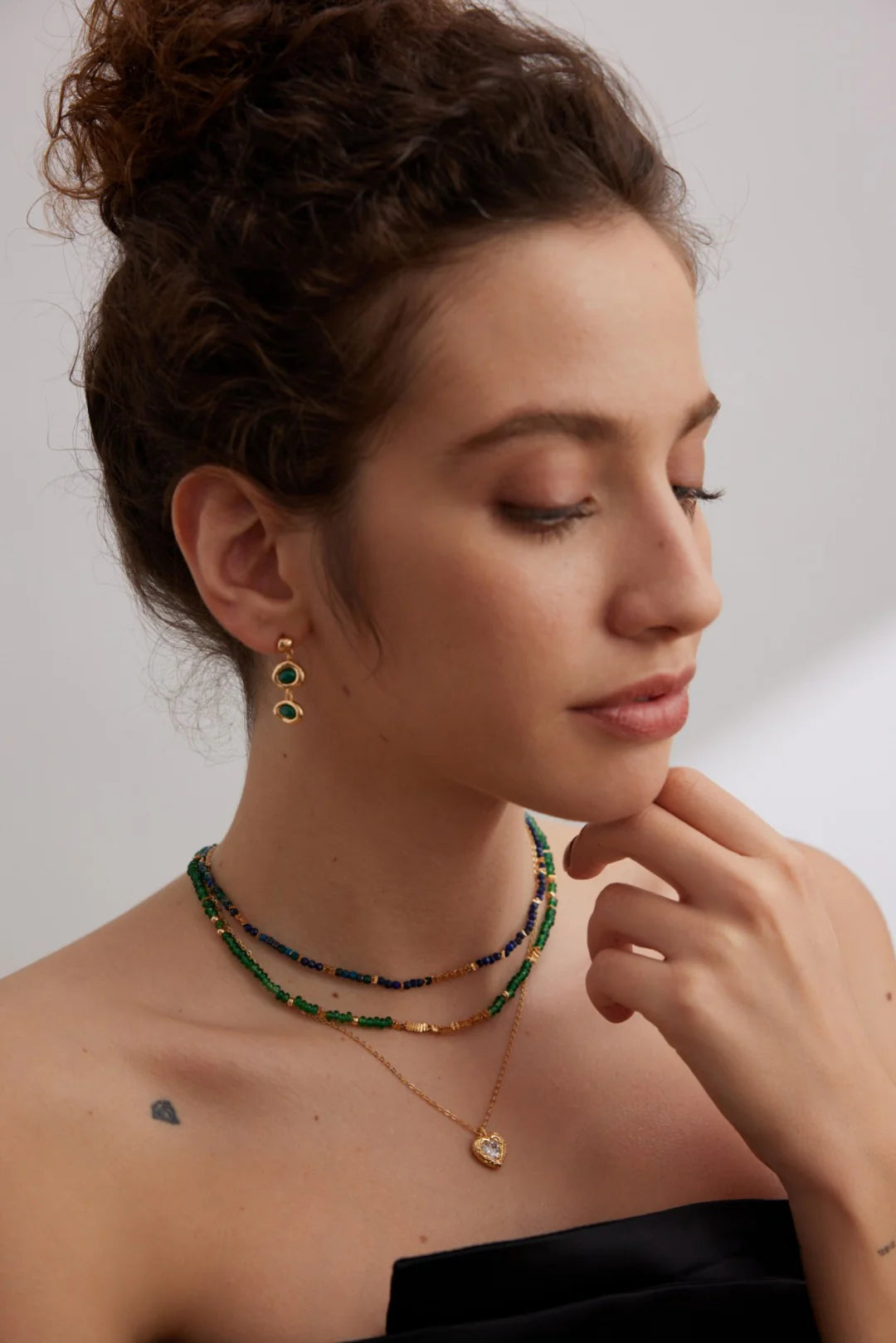 Model side profile wearing Anaïs & Aimee Emerald Green Choker with layered gold necklaces