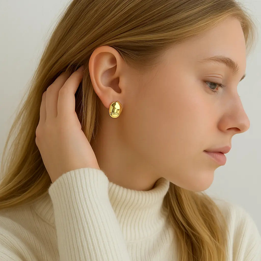Close-up side profile of blonde woman in cream turtleneck wearing gold stud earrings