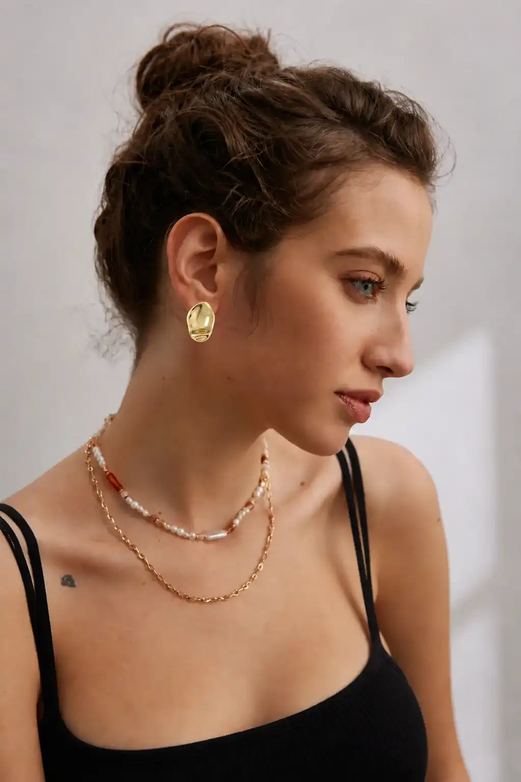 Model wearing Essence sculptural gold statement earrings with a polished organic finish.