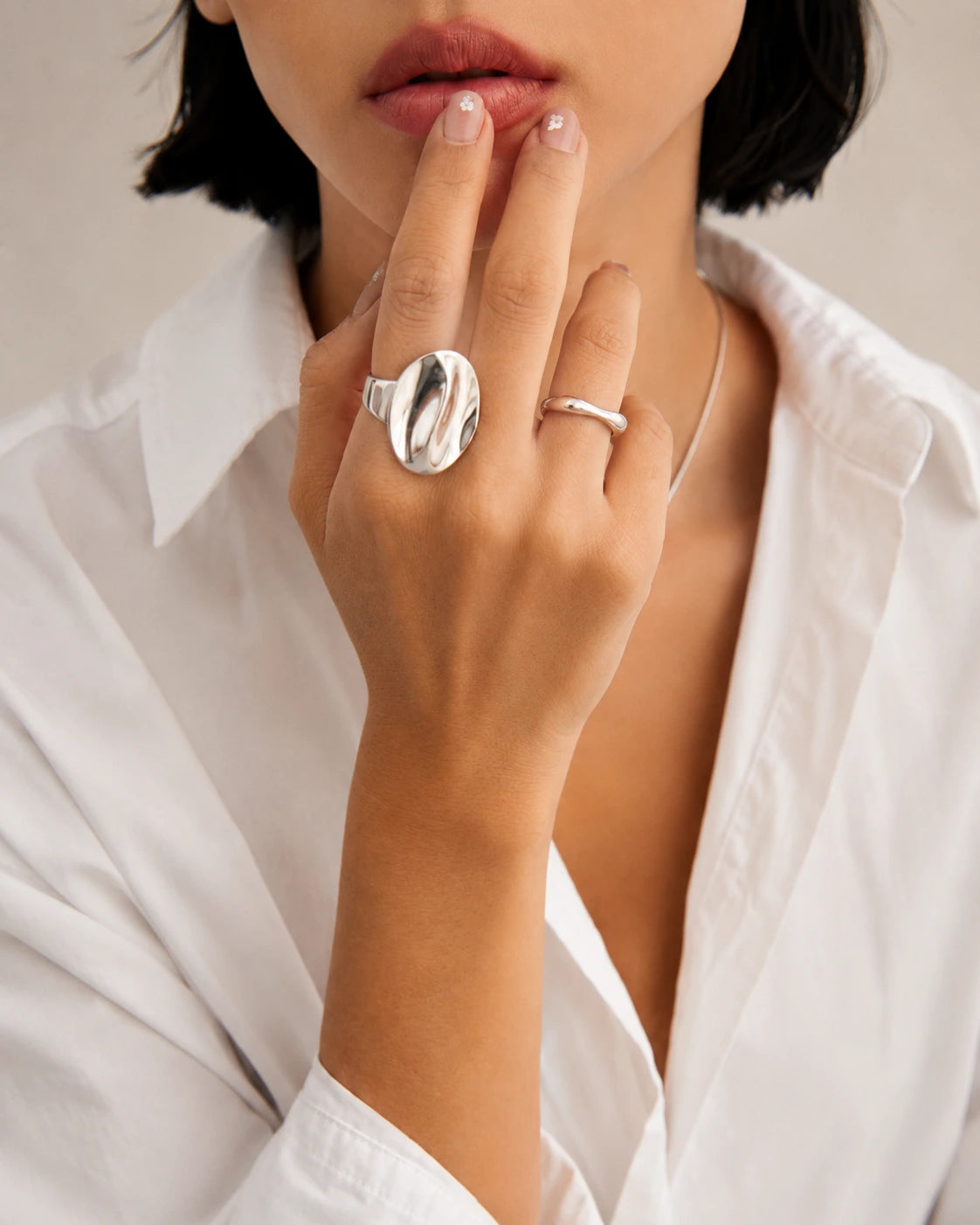 Close-up of a person wearing two silver rings on a neutral background