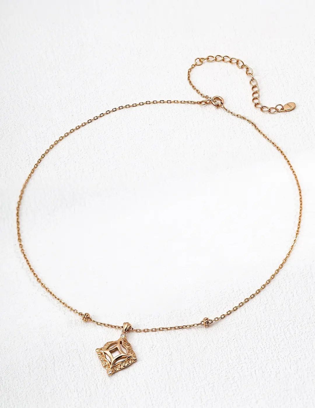 Gold square pendant necklace with intricate geometric detailing on a delicate adjustable chain displayed on a white background.