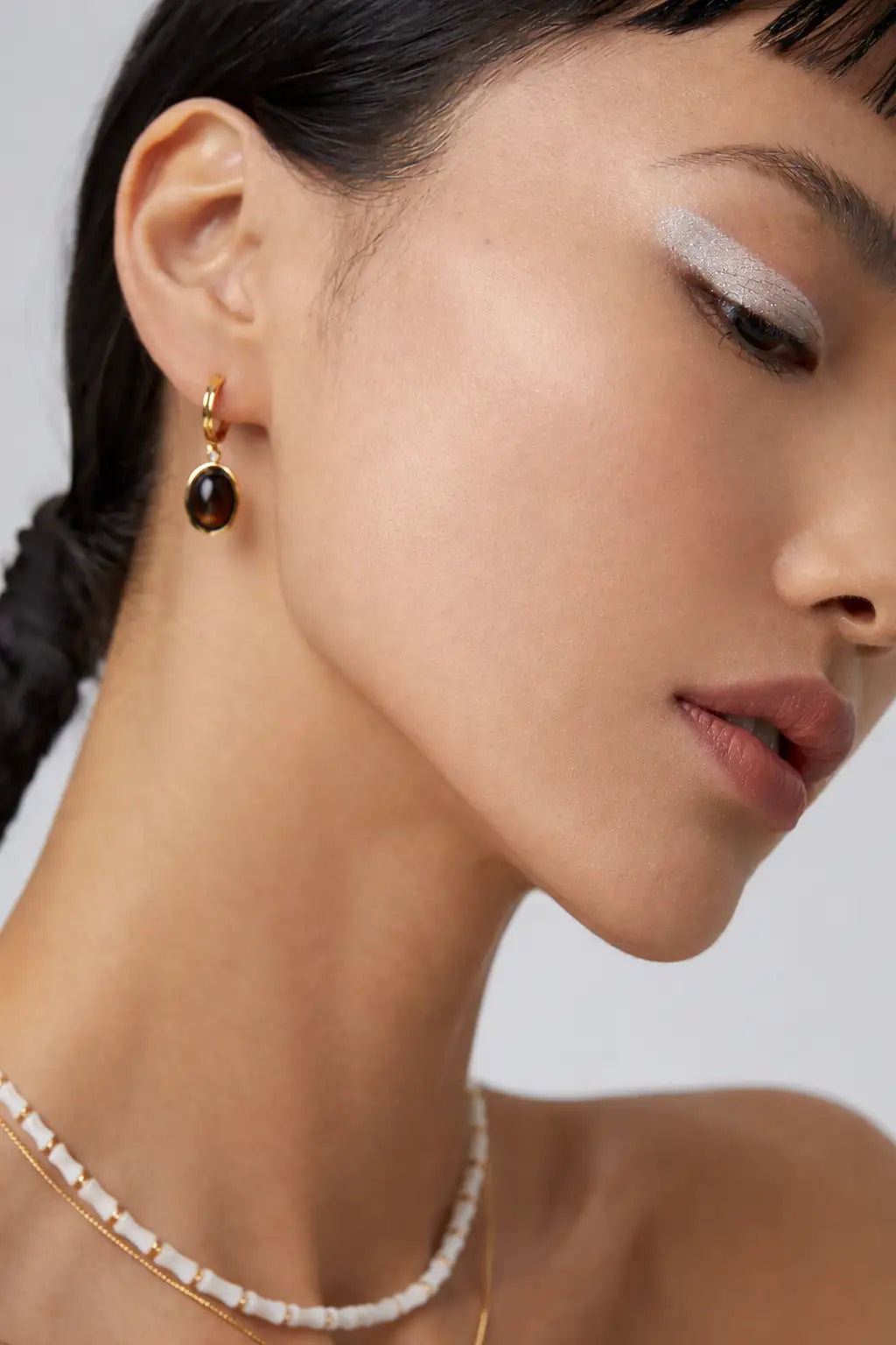 Close-up of a woman wearing gold earrings and a necklace against a neutral background