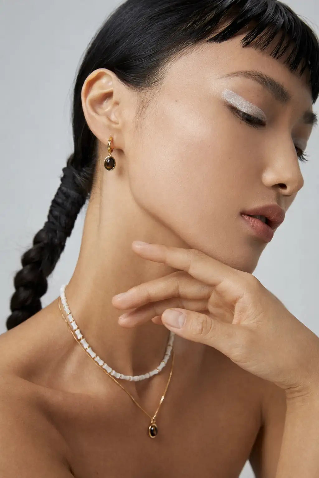 Woman wearing gold earrings and necklace against a neutral background