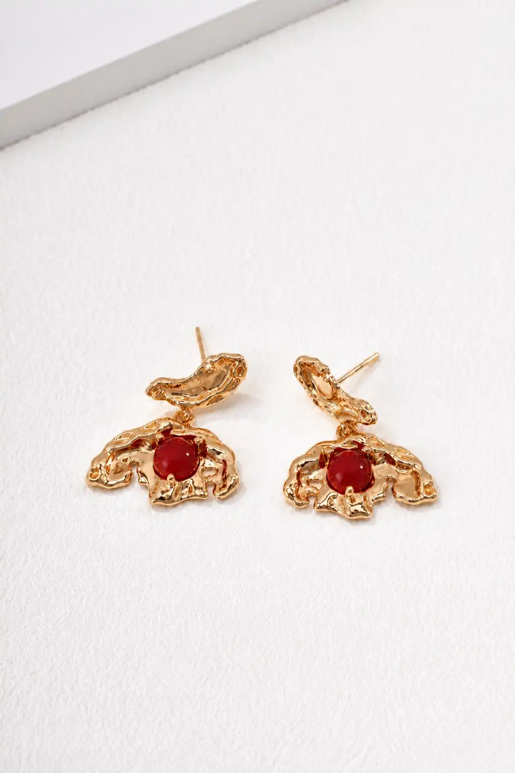 Close product view of the Hillmarton earrings featuring organic gold wings and round red agate stones under soft natural lighting.
