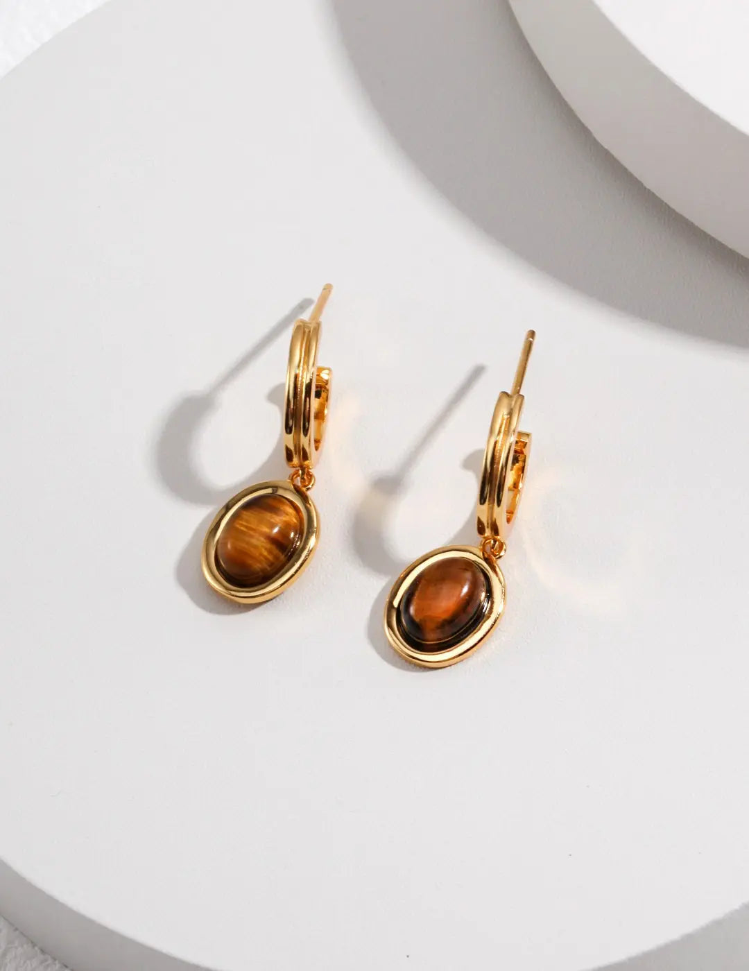 Gold earrings with tiger's eye stones on a white surface