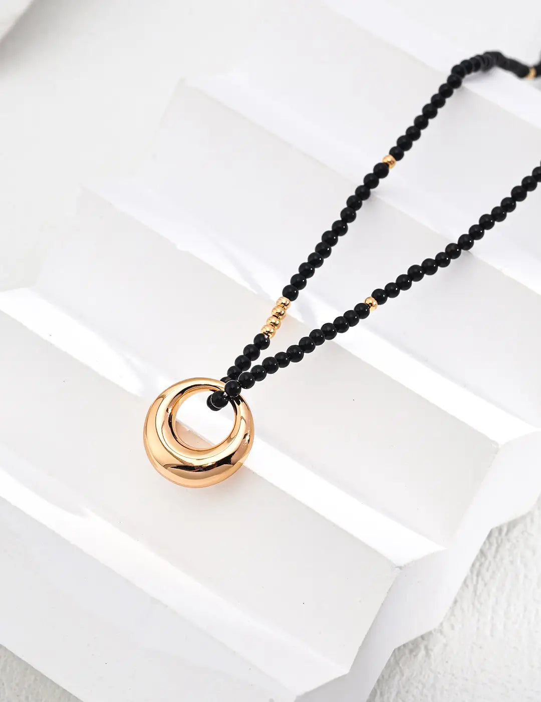 Model wearing Lunar Circle black agate necklace layered with gold chains for elegant style