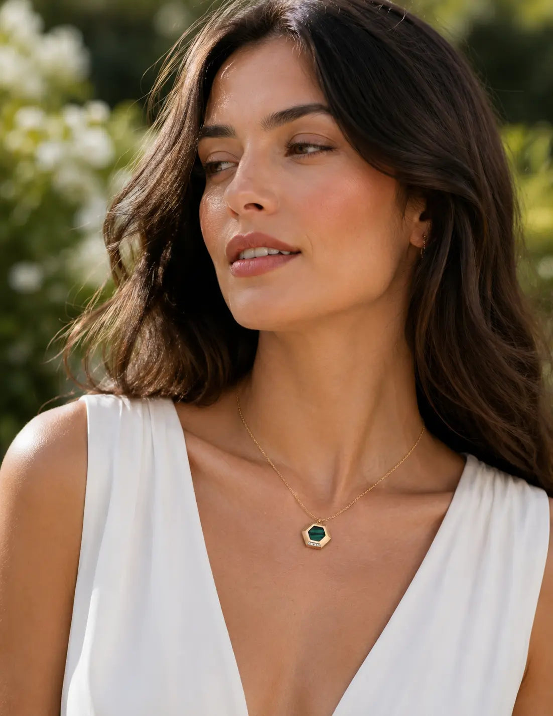 Woman wearing the Malachite Pendant Necklace, a vintage gold green stone necklace with natural malachite pendant, styled with a white outfit in soft natural light.