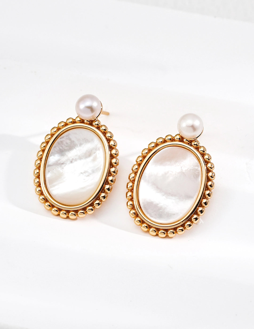 Pair of gold-framed earrings with pearl accents on a white background