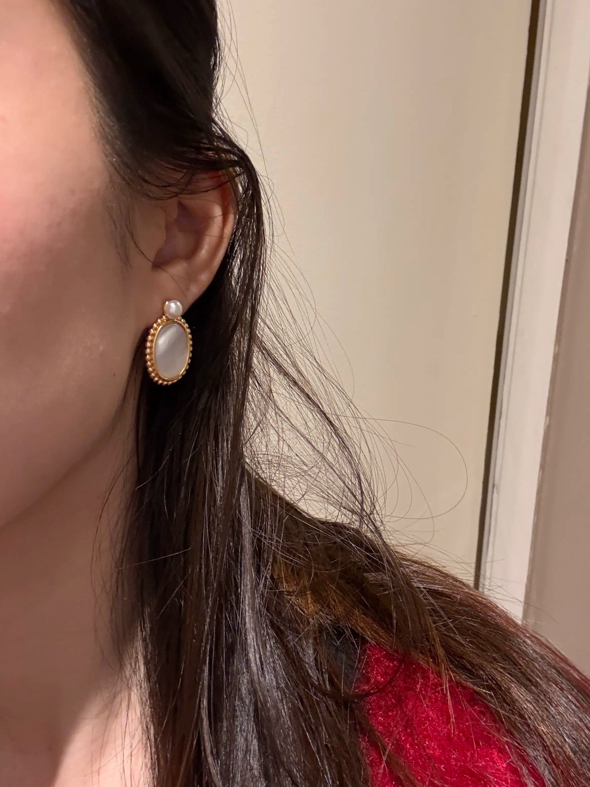 Close-up of an earring worn by a person with red hair, against a neutral background.