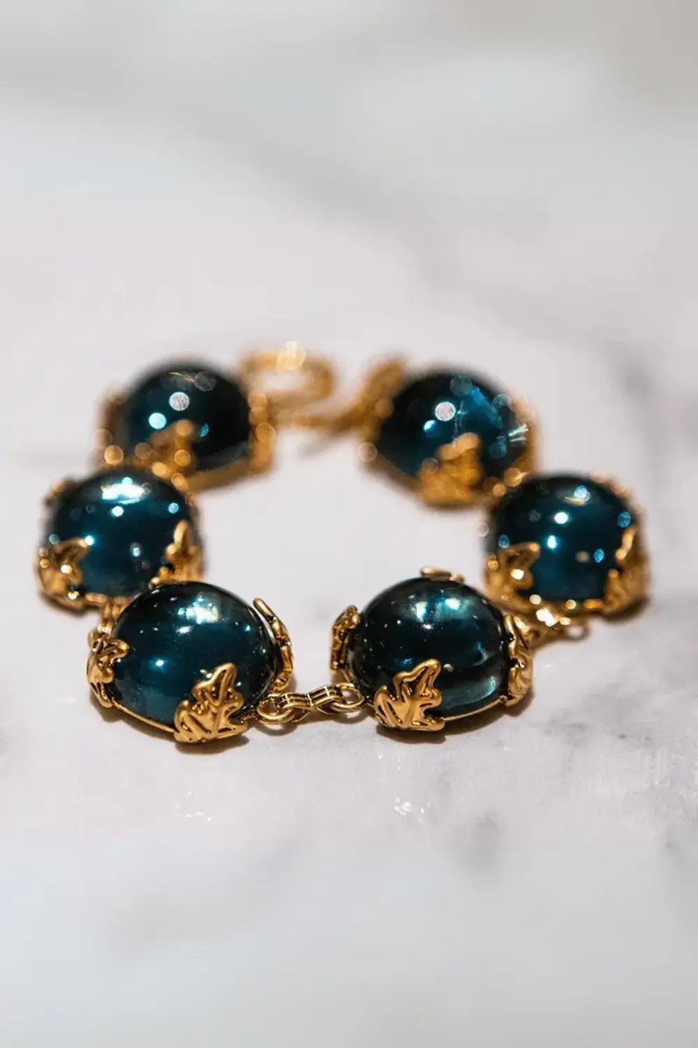 Close-up of Patchouli Bristol Blue Glass Bracelet with blue stones in gold leaf settings on marble