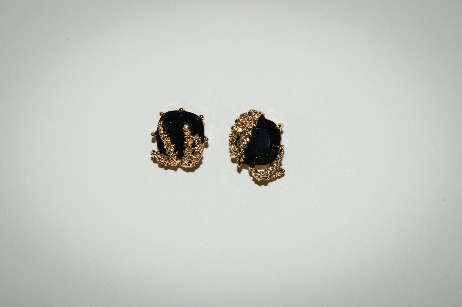 Close-up front view of Patchouli Flower Black Obsidian Stud Earrings with gold details.