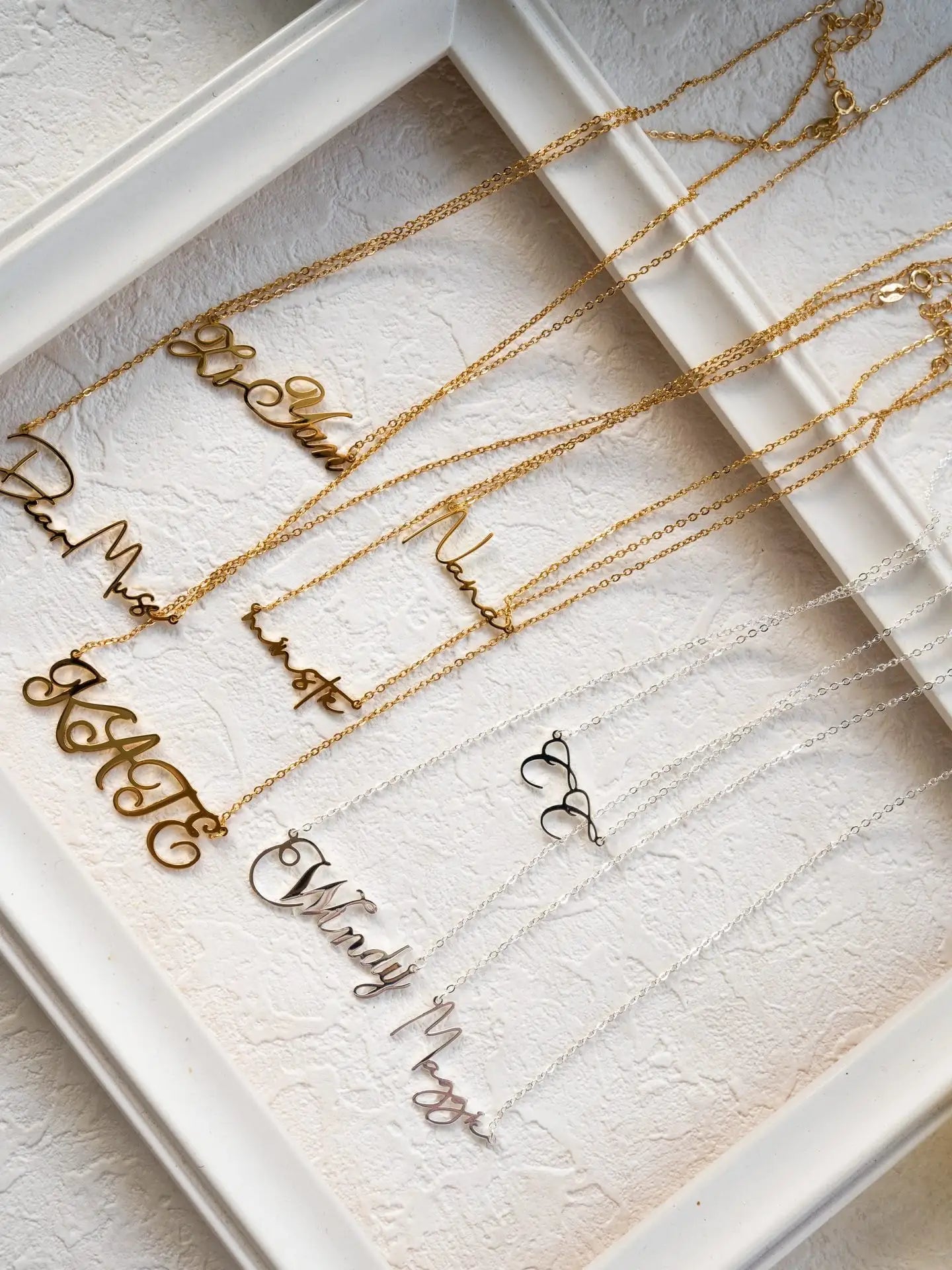 Gold necklaces with engraved names on a textured white surface
