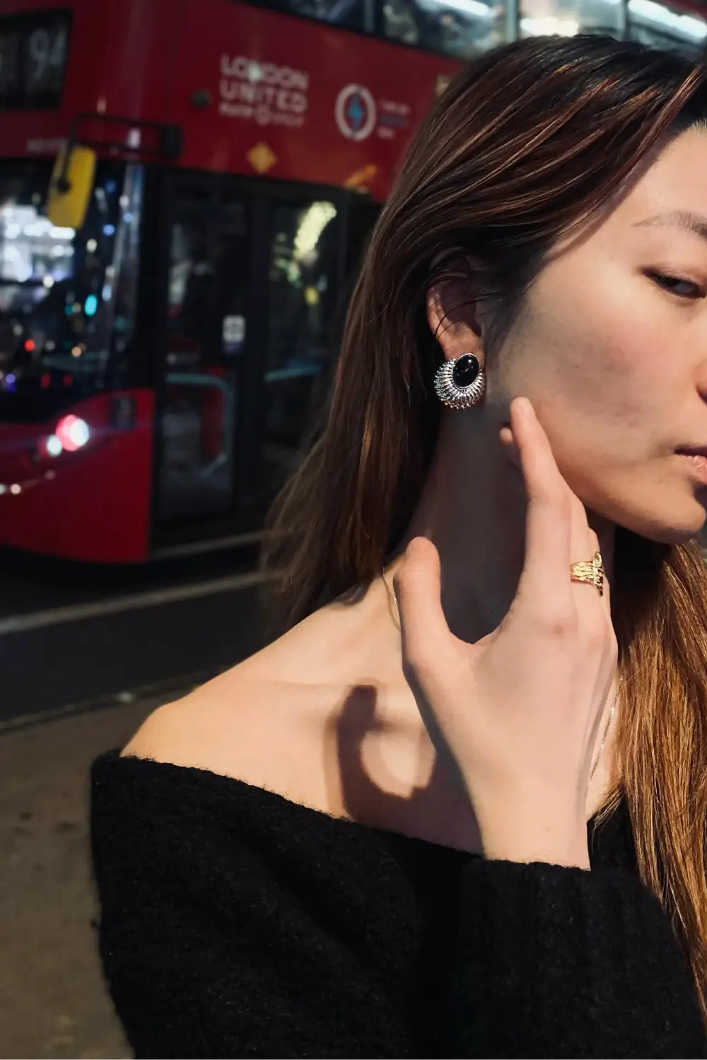 Woman wearing Anaïs & Aimee Serenity Black Onyx silver earrings by a red London bus at night