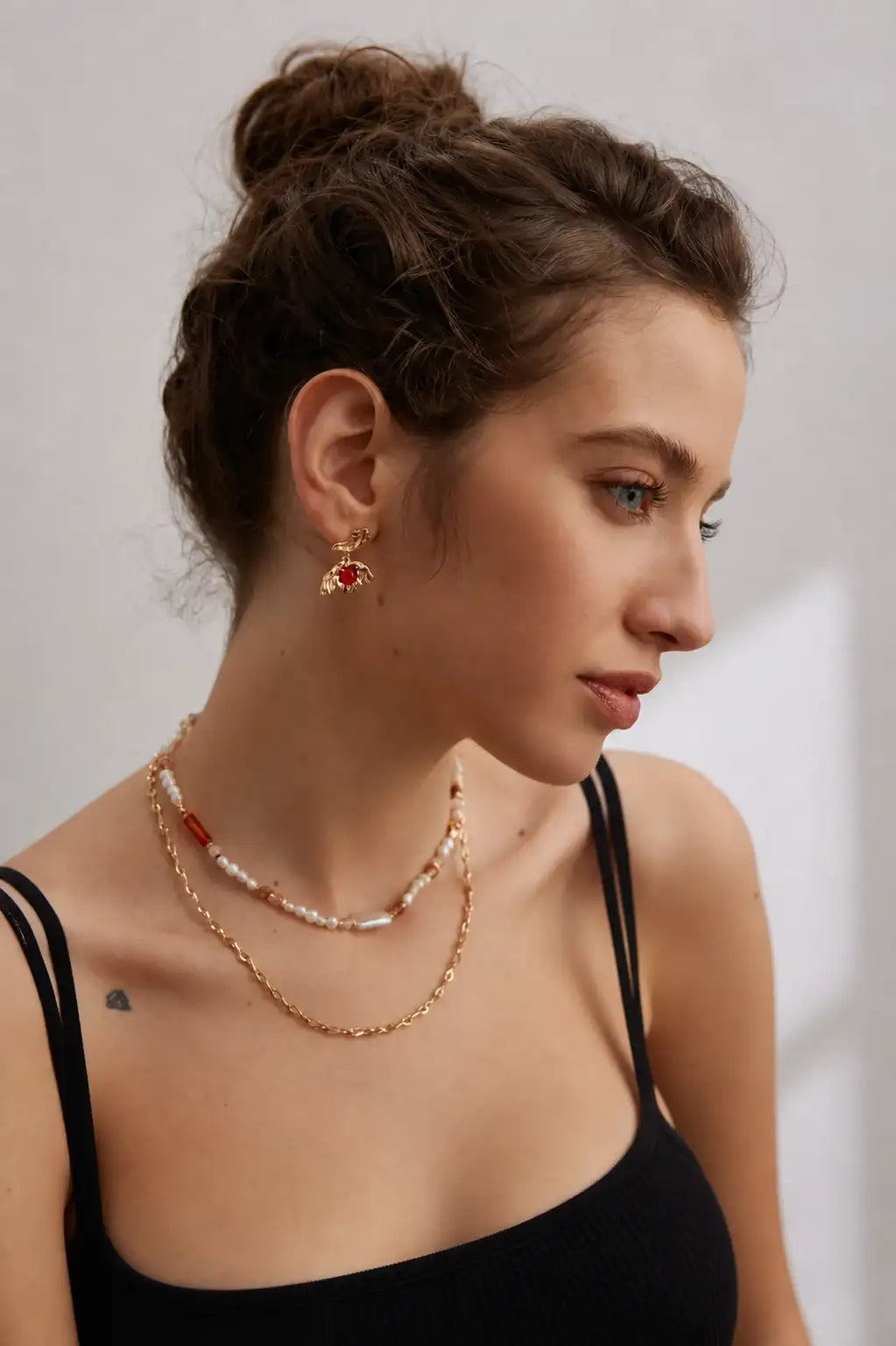 Lifestyle portrait of a model styling the Hillmarton gold butterfly earring with layered gold, pearl and gemstone necklaces.