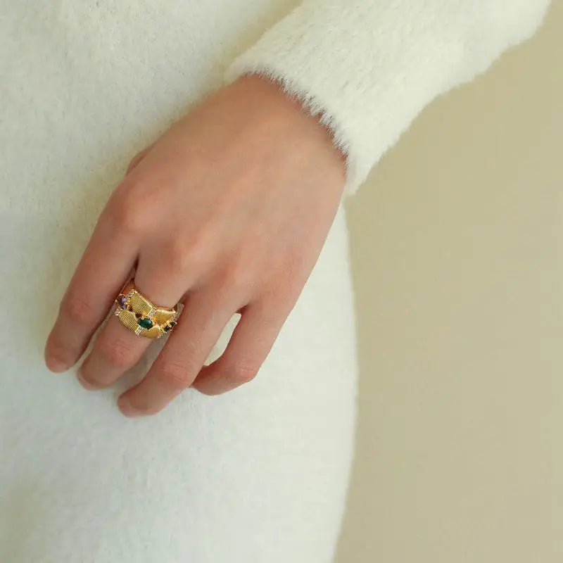 Close-up of hand wearing Tempestuous Hues gold hoops with green, purple, and red gemstones