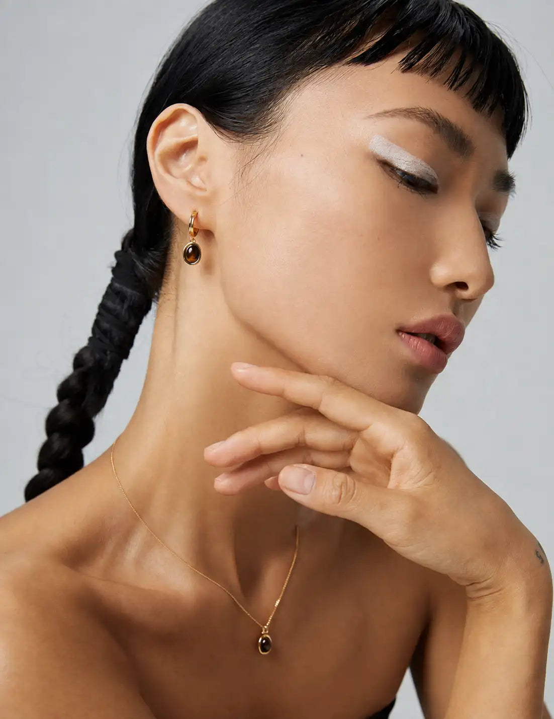 Model wearing a gold tiger’s eye pendant necklace with matching drop earrings