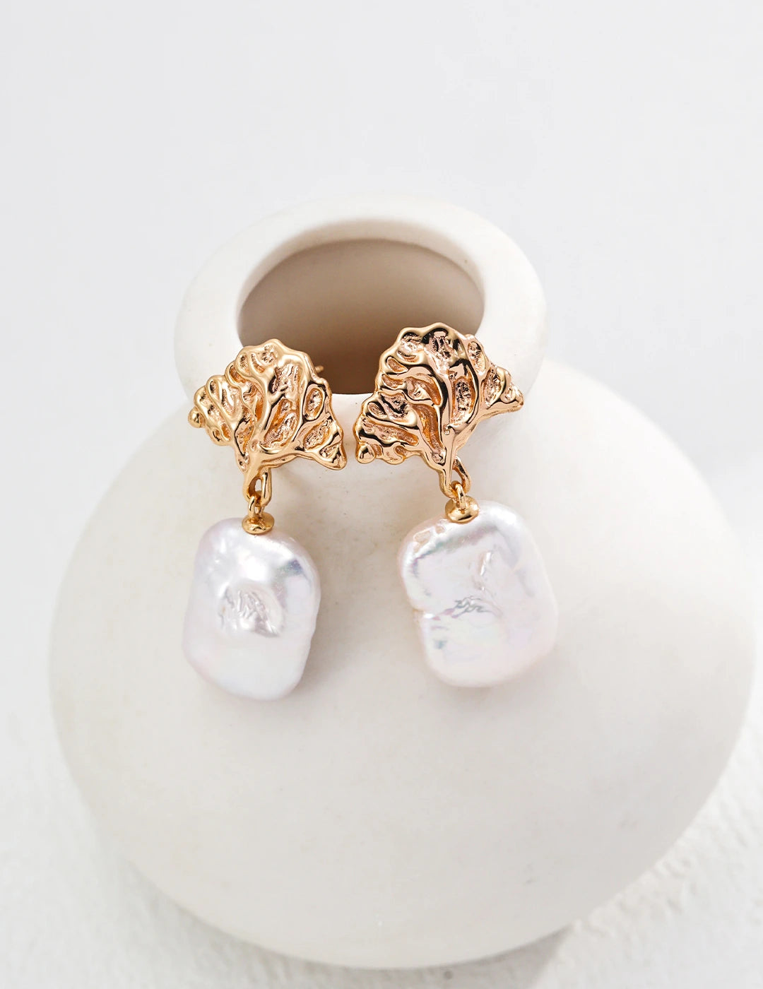 Gold and pearl earrings on a white stand with a white background