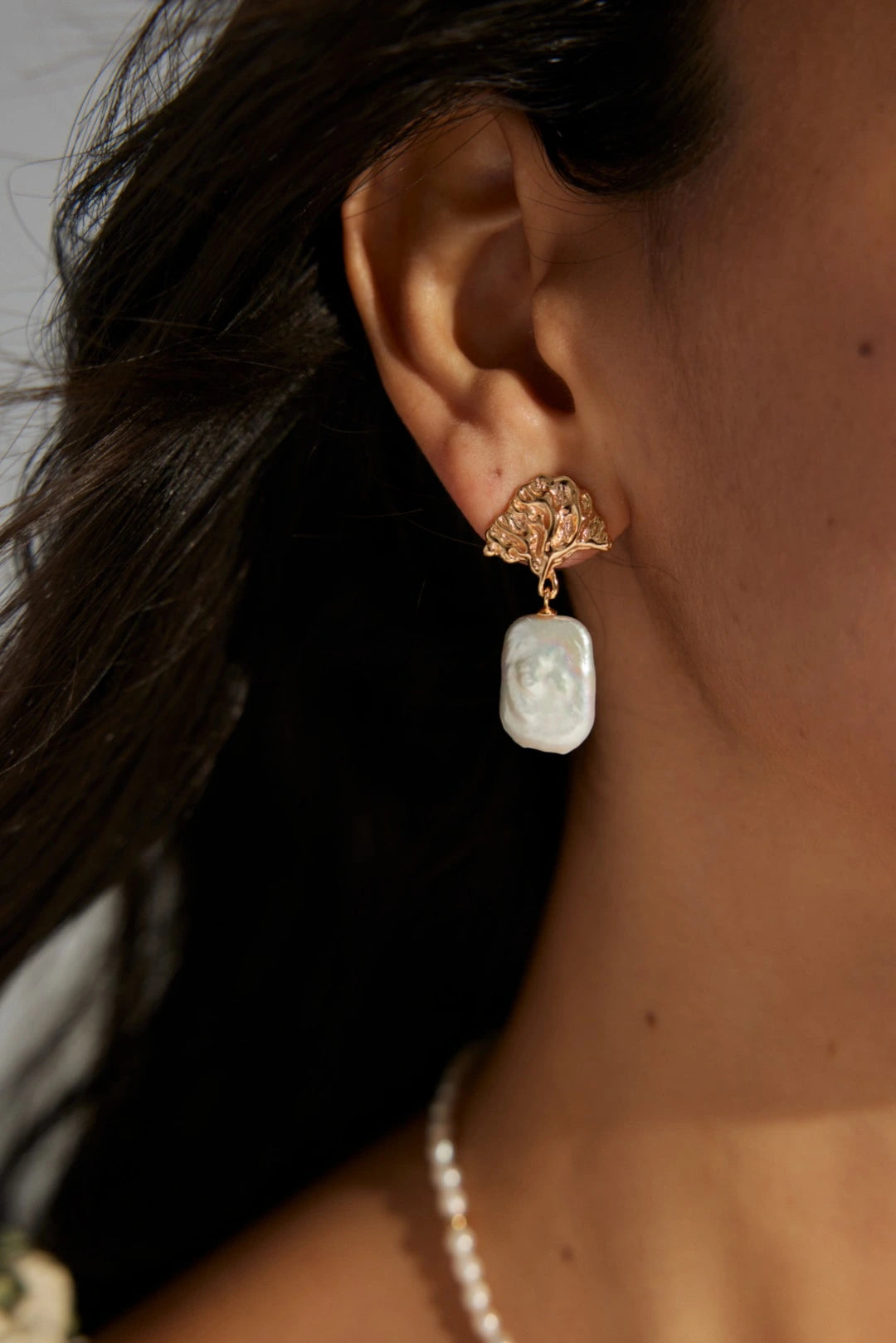 Close-up of a person wearing a gold earring with a white stone.