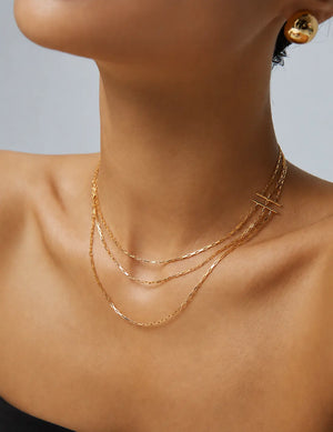 Gold necklaces on a person's neck against a neutral background