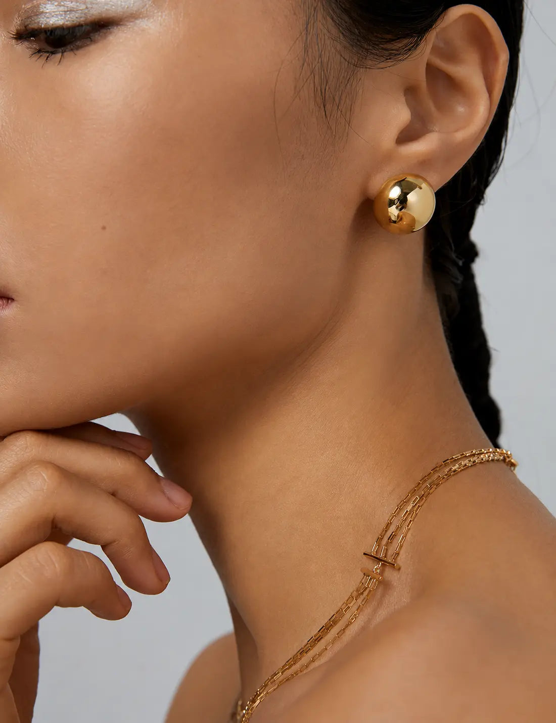 Close-up of a woman wearing gold earrings and a necklace against a neutral background