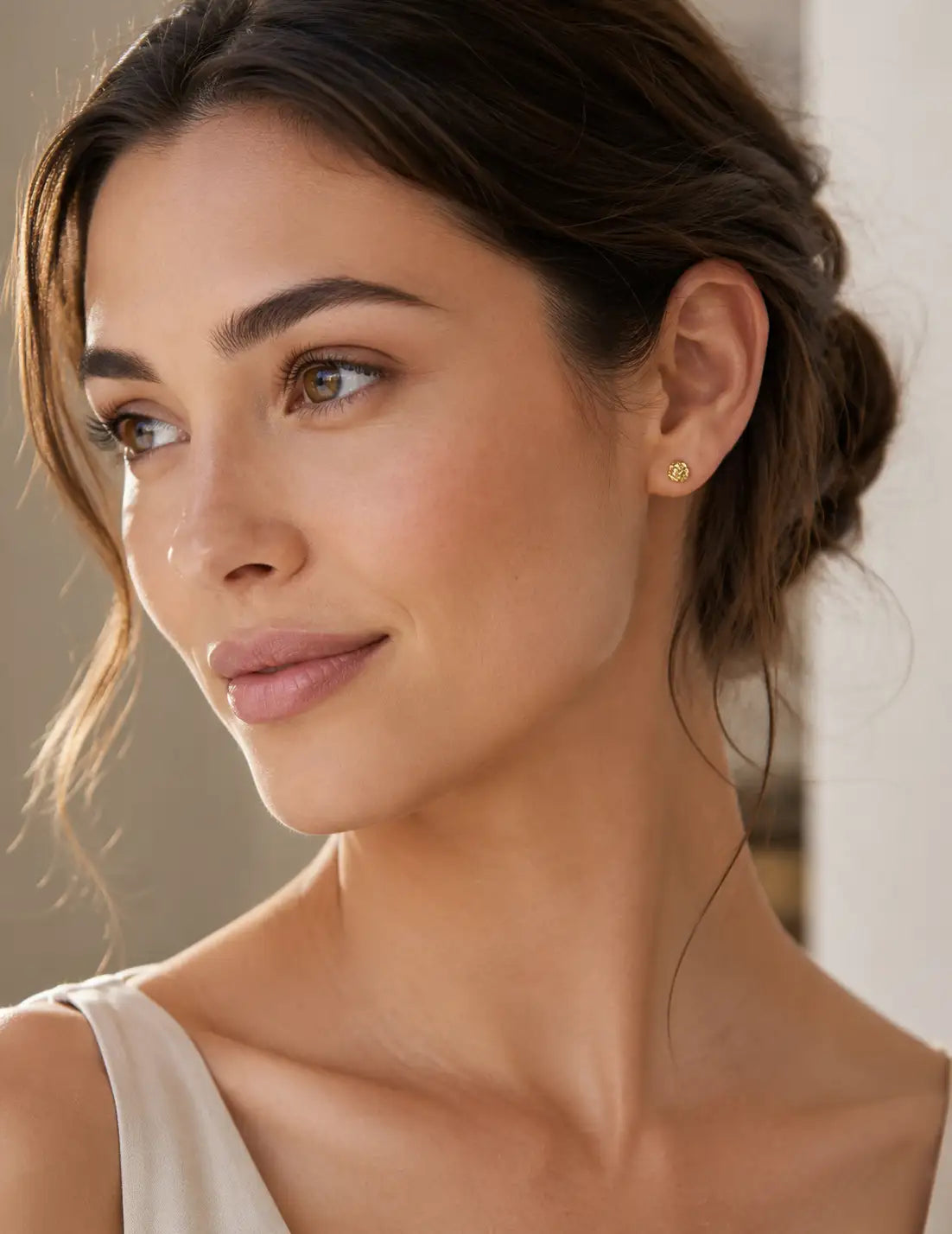 Elegant portrait of a woman wearing textured gold stud earrings, styled with soft makeup and a neutral outfit for a timeless jewellery look.