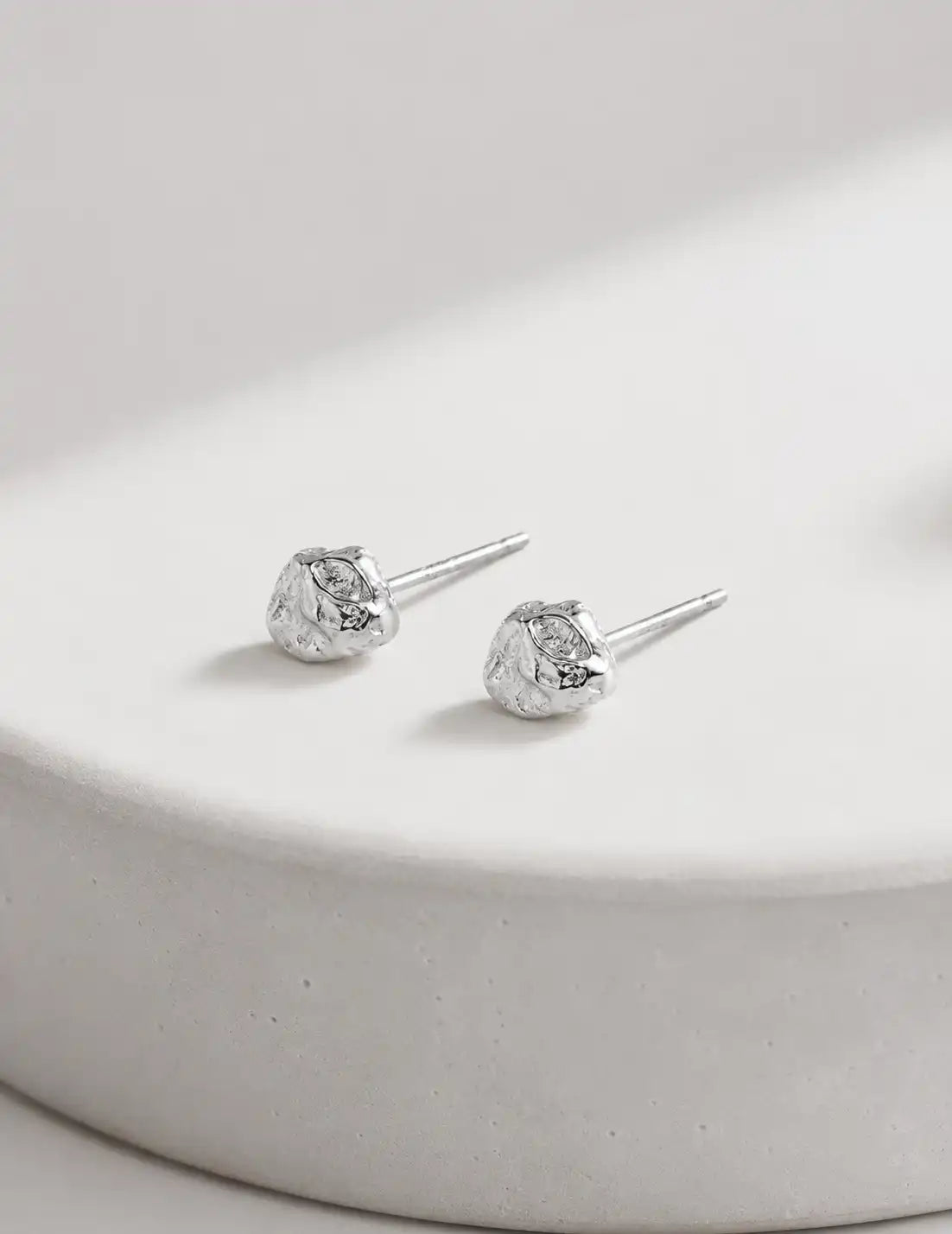 Close-up of a woman wearing textured silver stud earrings, styled with soft natural light and a clean neutral background for a minimalist jewellery look.
