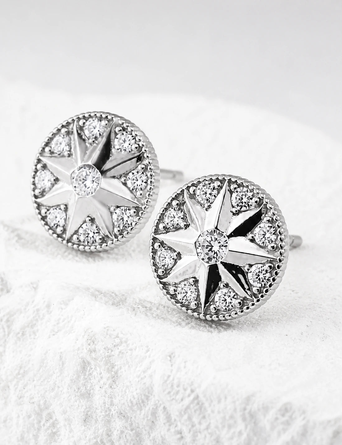 Pair of Didcot sterling silver starburst stud earrings with cubic zirconia, high three-quarter view.