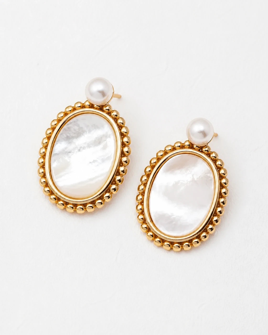 Top-down view of Haslemere gold mother of pearl drop earrings with luminous pearl studs and beaded oval frames