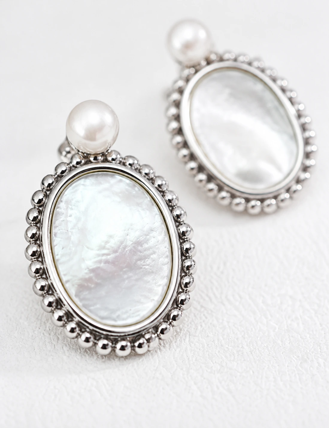 Close-up of Haslemere silver mother-of-pearl drop earrings with pearl studs and polished beaded oval frames