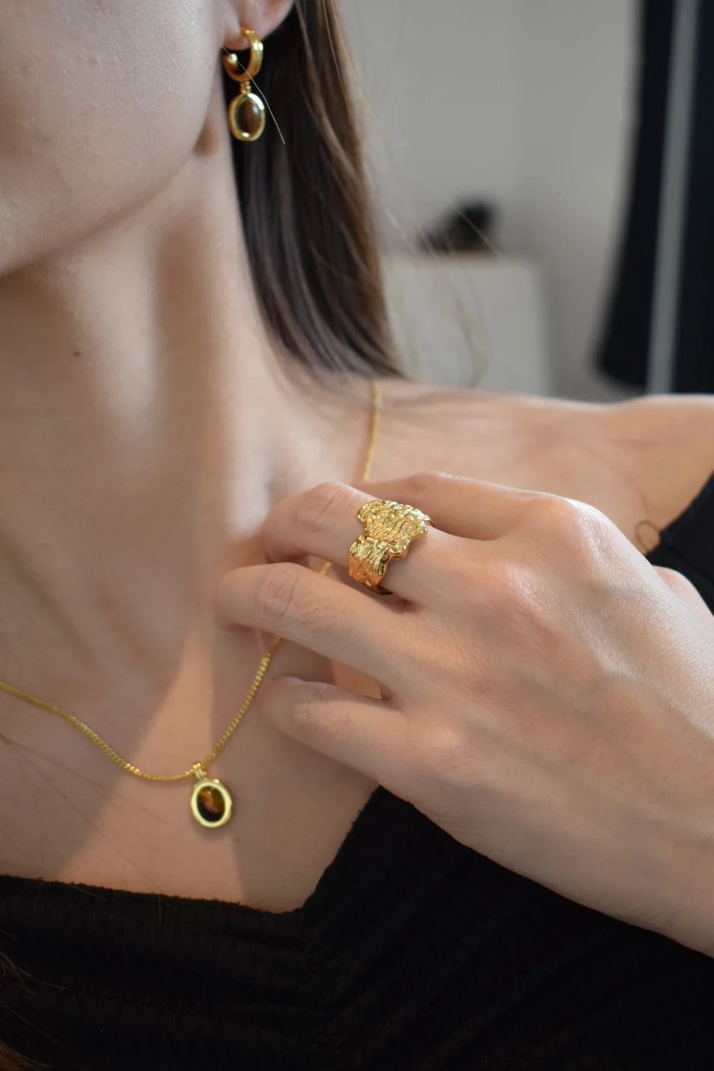 Close-up of model’s hand with Erosia gold ring, Tiger’s Eye necklace, and gold drop earrings.
